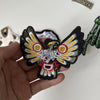 A hand holds a black embroidered patch featuring a stylized eagle with yellow and white feathers and red accents.