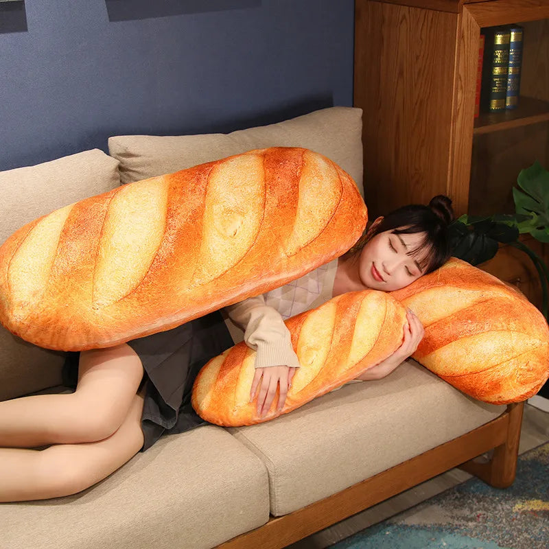 An orange French bread plush pillow resting on a beige sofa.
