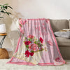 A pink floral print throw blanket featuring a 'best mom ever' design draped over a beige sofa.