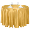 A round table set with a golden satin tablecloth, glassware, and silverware.