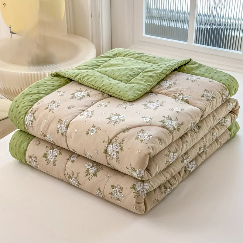 A stack of lightweight floral printed summer quilts in beige and light green fabric.