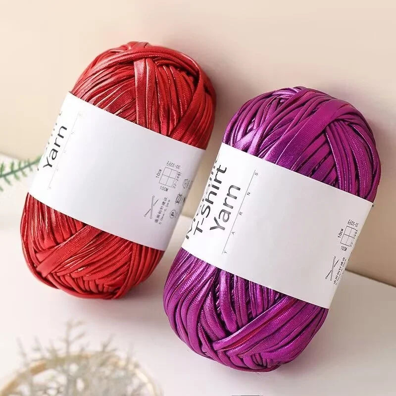 Two skeins of metallic fabric strip yarn in red and purple are displayed on a white surface.