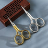 A pair of vintage stainless steel sewing scissors with gold accents resting on a dark wooden box.