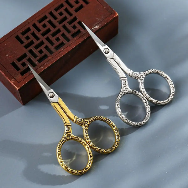 A pair of vintage stainless steel sewing scissors with gold accents resting on a dark wooden box.