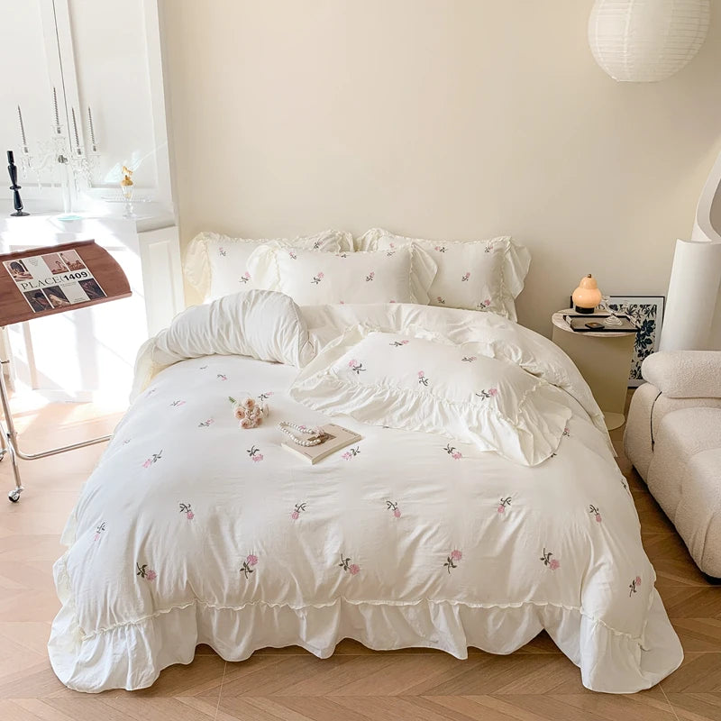 A white duvet cover set with pink embroidered roses displayed on a bed in a bright room.