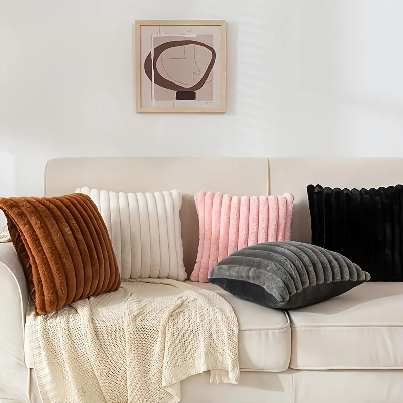 A collection of striped corduroy pillow covers in shades of brown, pink, and gray displayed on a light-colored sofa.