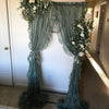 A sheer floral lace curtain panel in sage green hangs as a decorative backdrop.