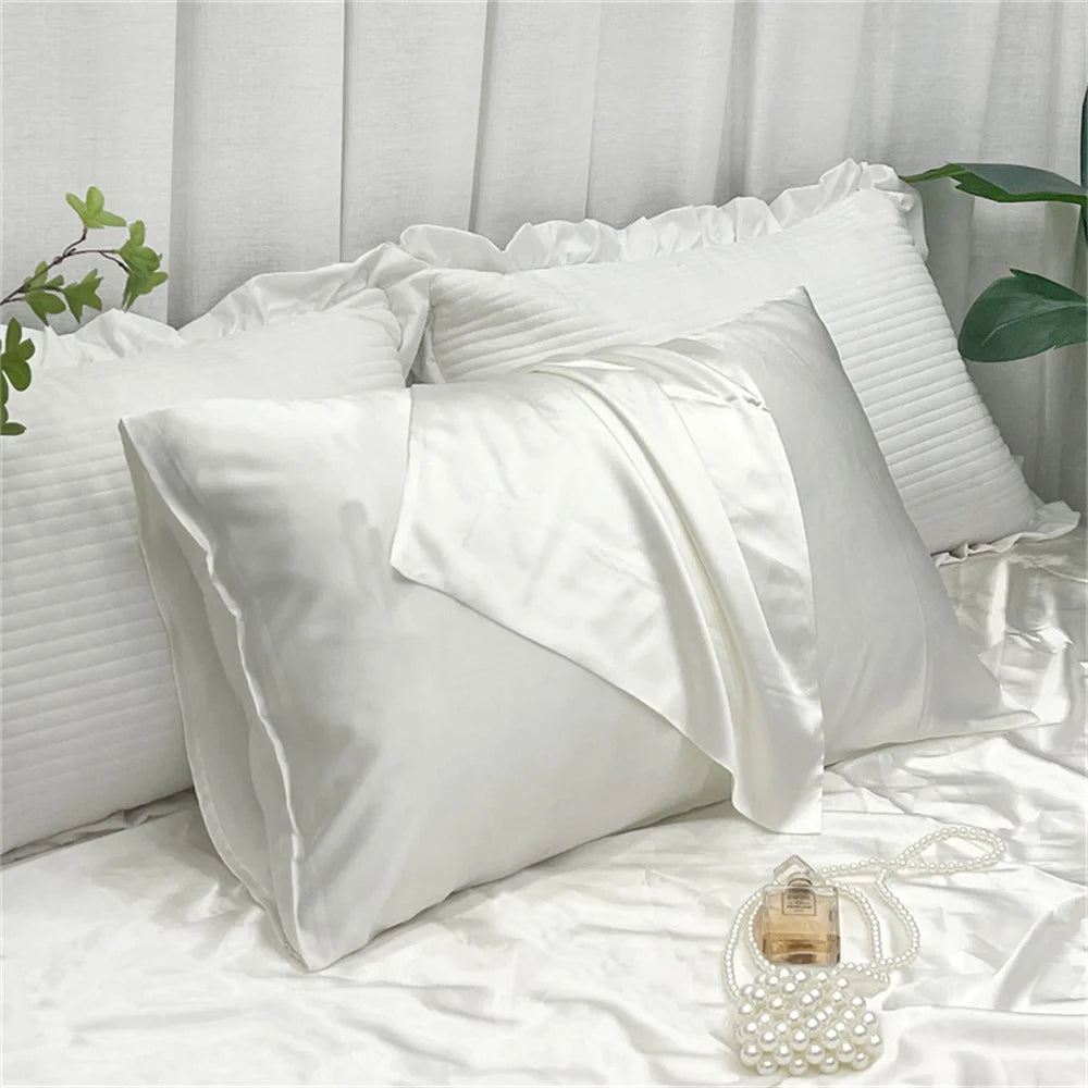 White satin pillowcases and a decorative pearl accessory on white bedding.