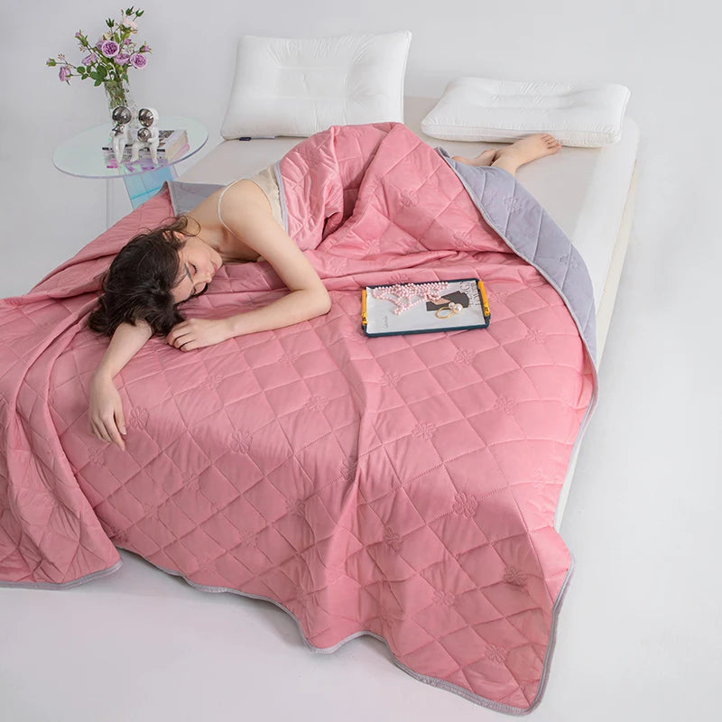 A woman lies comfortably on a pink quilted blanket indoors with white pillows and a small book.