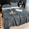 A thick gray knitted blanket with vertical stripes is draped over a bed, featuring a textured, fluffy appearance.