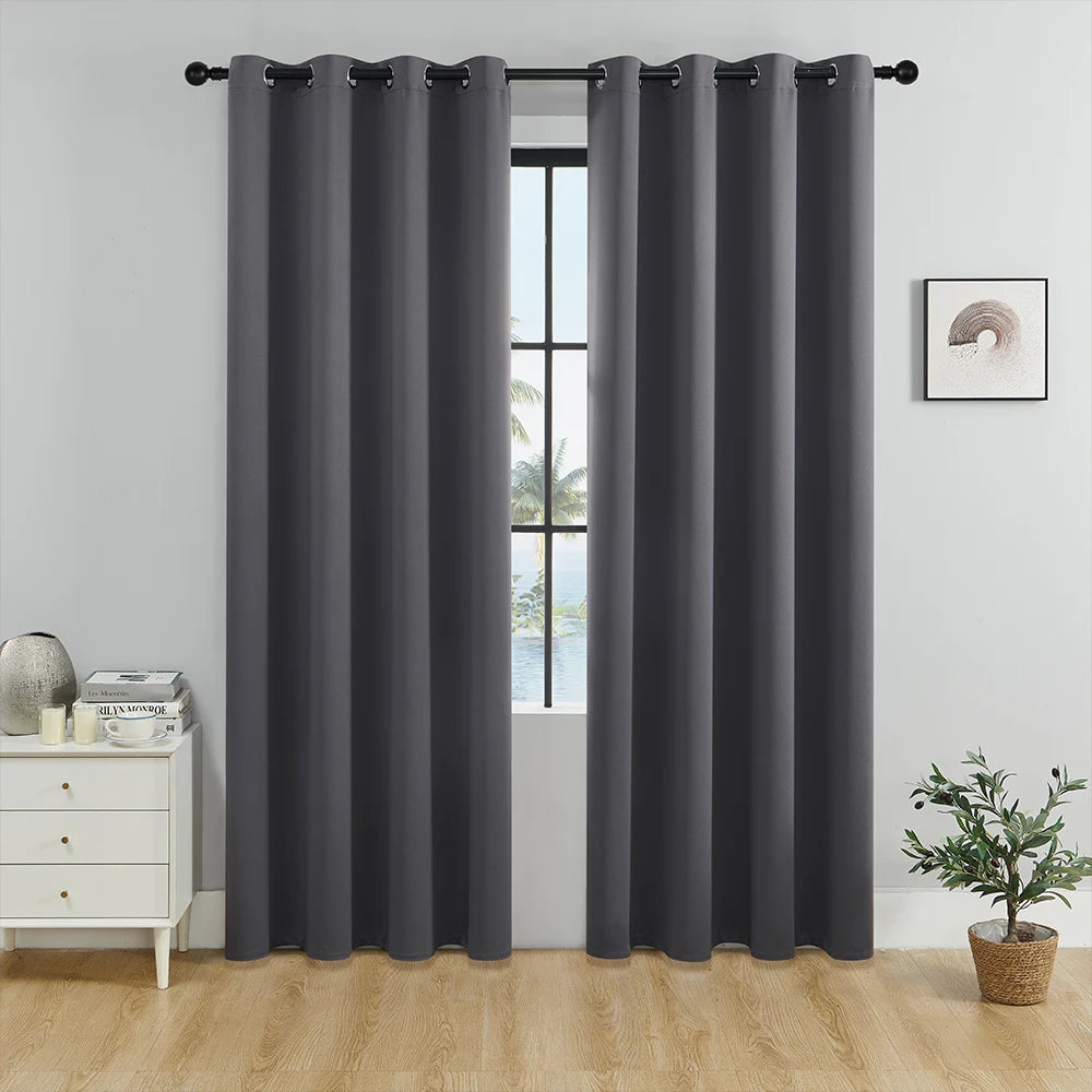 A set of solid gray blackout window curtains hanging on a rod in a bright room.