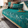 A teal velvet sofa cover with gold leaf pattern displayed on a bed, featuring decorative pillows and a gold tray.