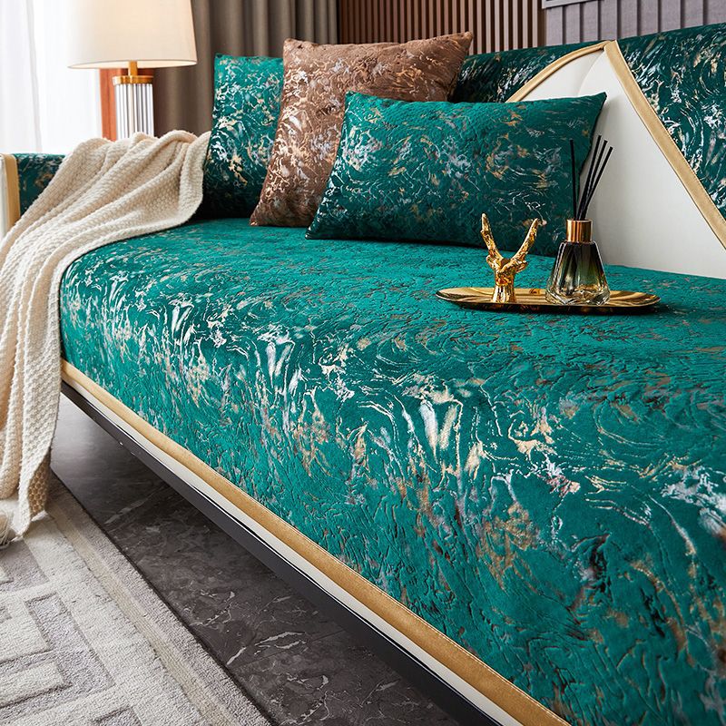A teal velvet sofa cover with gold leaf pattern displayed on a bed, featuring decorative pillows and a gold tray.