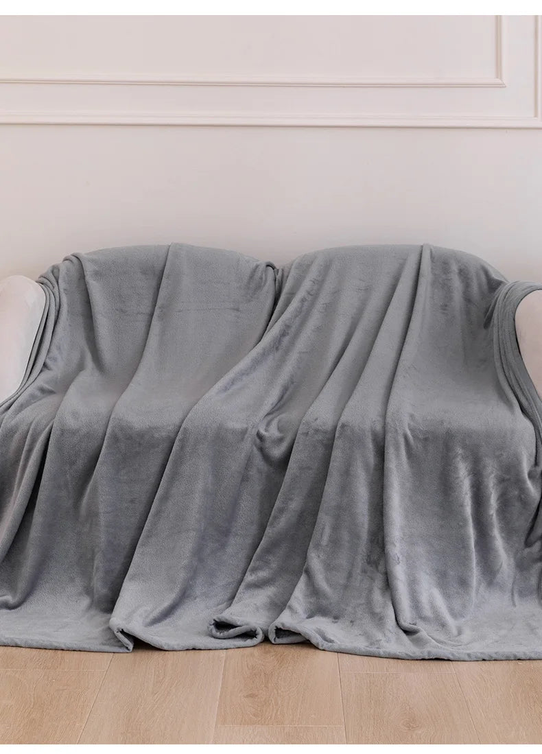 A soft gray flannel throw blanket draped over a white surface against a light wall.