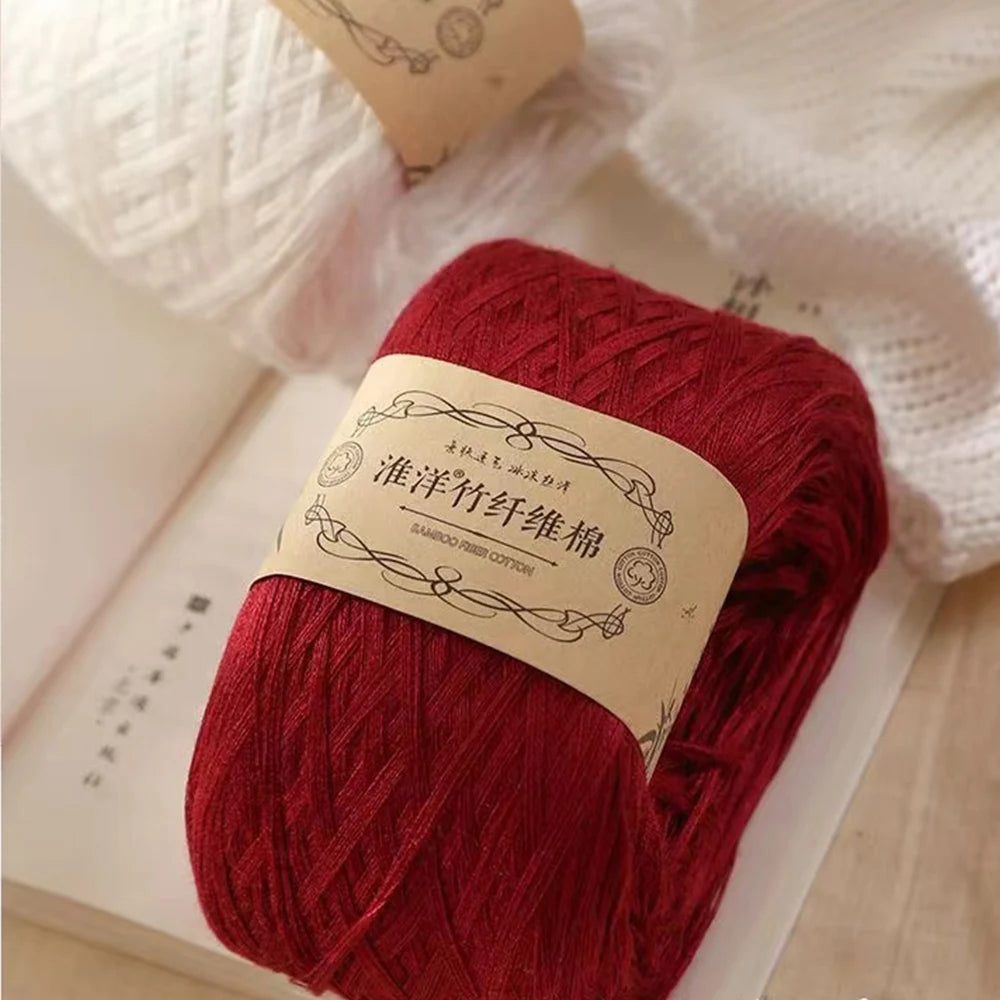 A ball of deep red yarn labeled as premium 100% cotton yarn for crafting resting on a light surface.