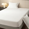 A white fitted sheet is placed on a bed, with a white pillow and a bedside lamp visible.