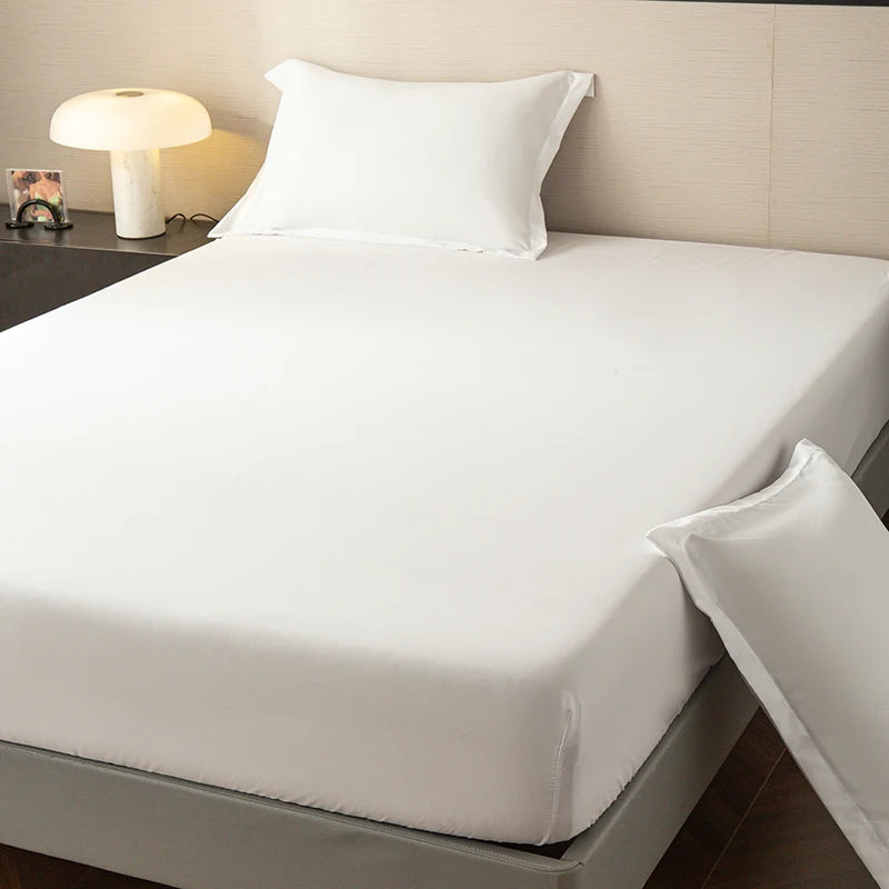 A white fitted sheet is placed on a bed, with a white pillow and a bedside lamp visible.