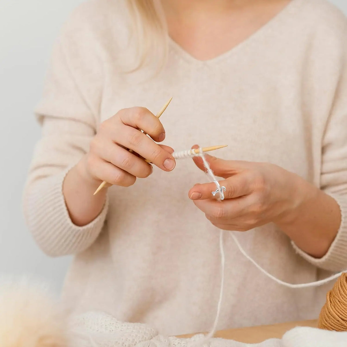 A person is using a crochet needle to create a loop ring from white yarn.