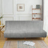 A modern gray velvet armless sofa cover displayed on a wooden floor with a patterned rug.