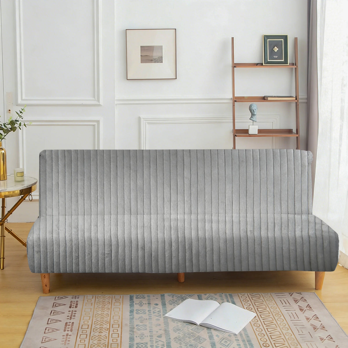 A modern gray velvet armless sofa cover displayed on a wooden floor with a patterned rug.