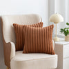 A brown faux fur stripe decorative throw pillow cover resting on a cream upholstered armchair.