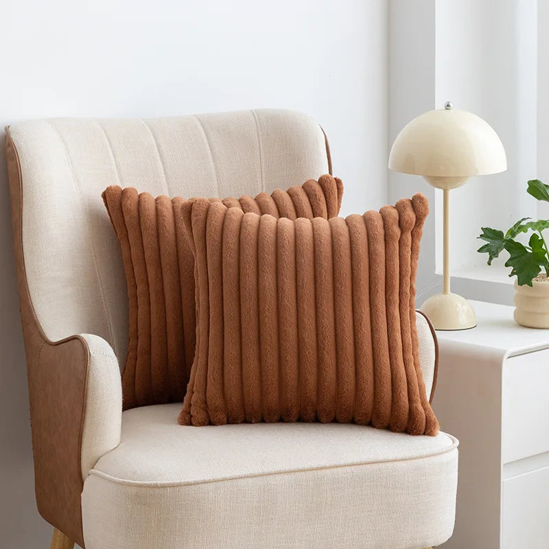 A brown faux fur stripe decorative throw pillow cover resting on a cream upholstered armchair.