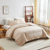 A beige quilted cotton bedspread set with matching pillows on a white bed in a bright room.