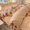 A bed with a pink bedding set featuring plaid patterns and embroidered animals.
