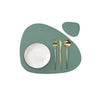 A set of gold-toned cutlery resting on a light green, organic-shaped placemat.