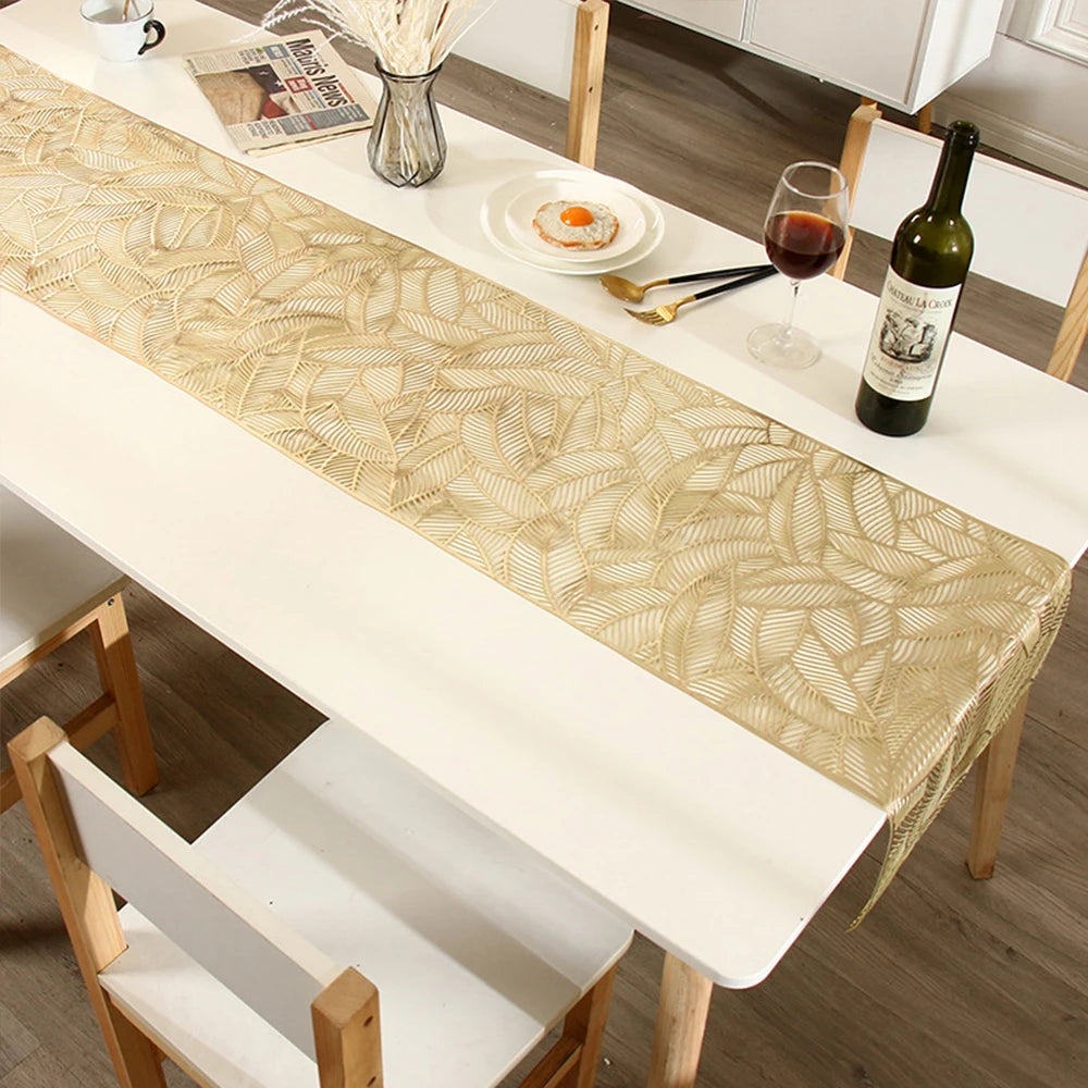 A long gold patterned table runner is displayed on a white dining table set for an event.