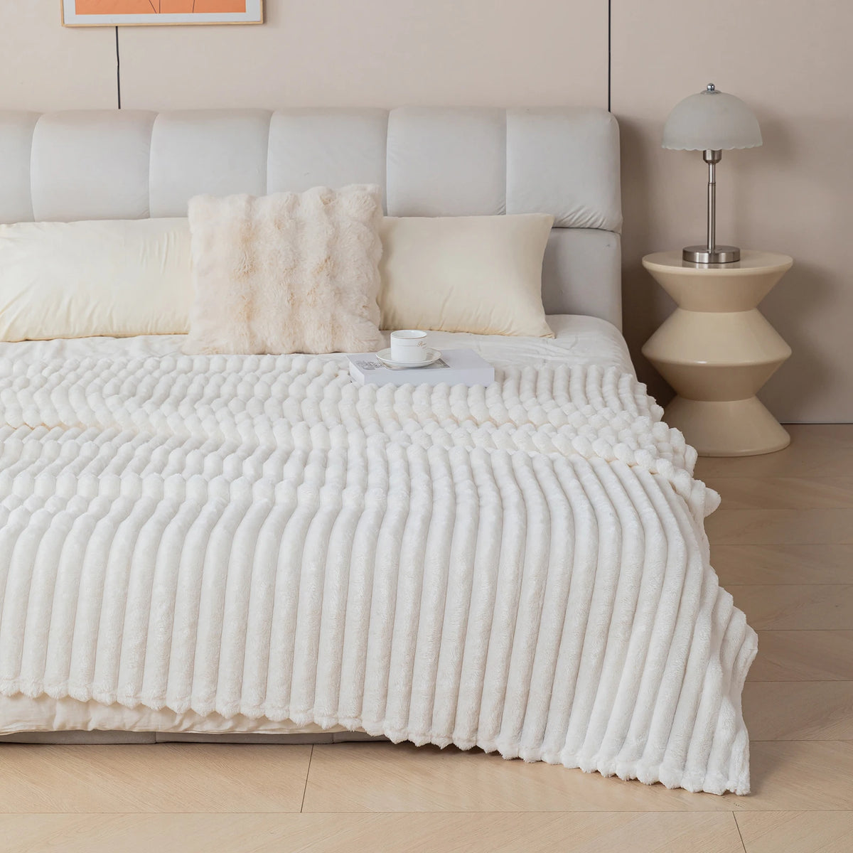A white soft flannel throw blanket is draped over a bed with light beige bedding and pillows.