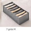 A gray foldable drawer organizer with seven fabric dividers for storing undergarments and accessories.
