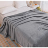 A gray extra soft flannel throw blanket draped over a white bed with a green stuffed animal nearby.