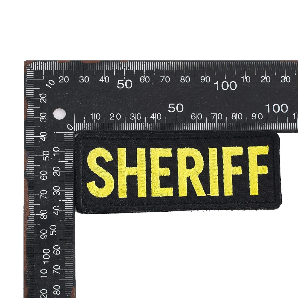 Black embroidered patch with the word SHERIFF in yellow thread against a ruler scale.