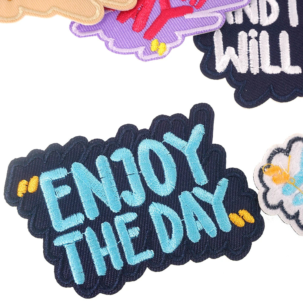 A collection of iron-on embroidered text patches in various colors including purple, red, and blue.