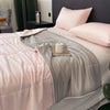 A pink and gray reversible cooling quilt is displayed on a bed with soft pillows.
