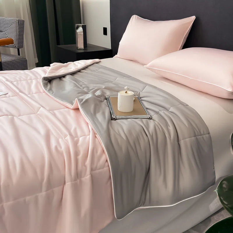A pink and gray reversible cooling quilt is displayed on a bed with soft pillows.