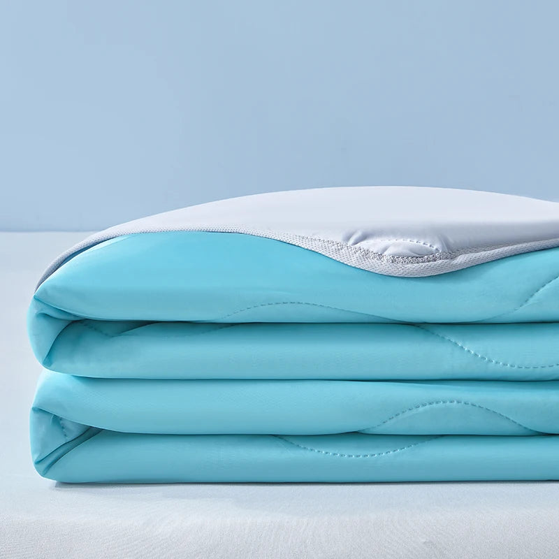 A stack of light blue cooling fiber blankets folded neatly on a white surface.