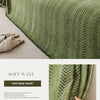 A close-up of a moss green textured fabric with an elegant fishbone pattern, shown draped on a light beige surface.