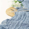 Light blue cheesecloth fabric draped with silver cutlery and a woven mat for boho decor