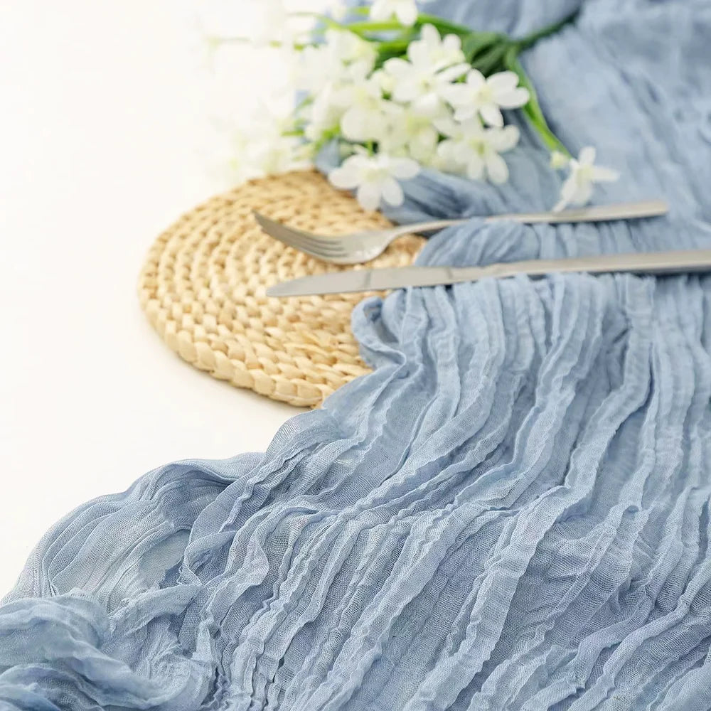 Light blue cheesecloth fabric draped with silver cutlery and a woven mat for boho decor