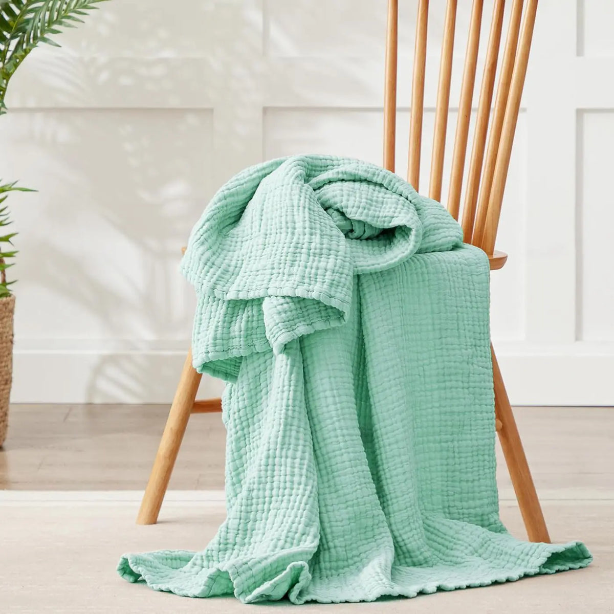 A light mint green ultra-soft 100% cotton gauze blanket draped over a wooden chair.