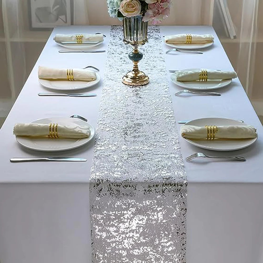 A white table set with gold-edged napkins and silverware, featuring a silver sequin glitter table runner.