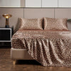 A leopard print satin bed sheet set displayed on a bed with neutral bedding and modern furniture.