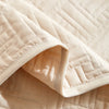A close-up of a beige quilted cotton bedspread fabric showing the diamond stitching pattern.
