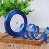 Roll of blue satin ribbon with a white core and several unrolled ribbons on a wooden surface