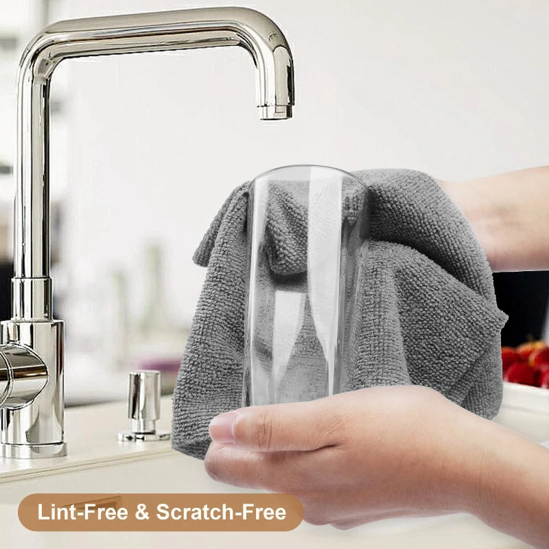 A hand is wiping a stainless steel kitchen faucet with a gray microfiber cleaning wipe.