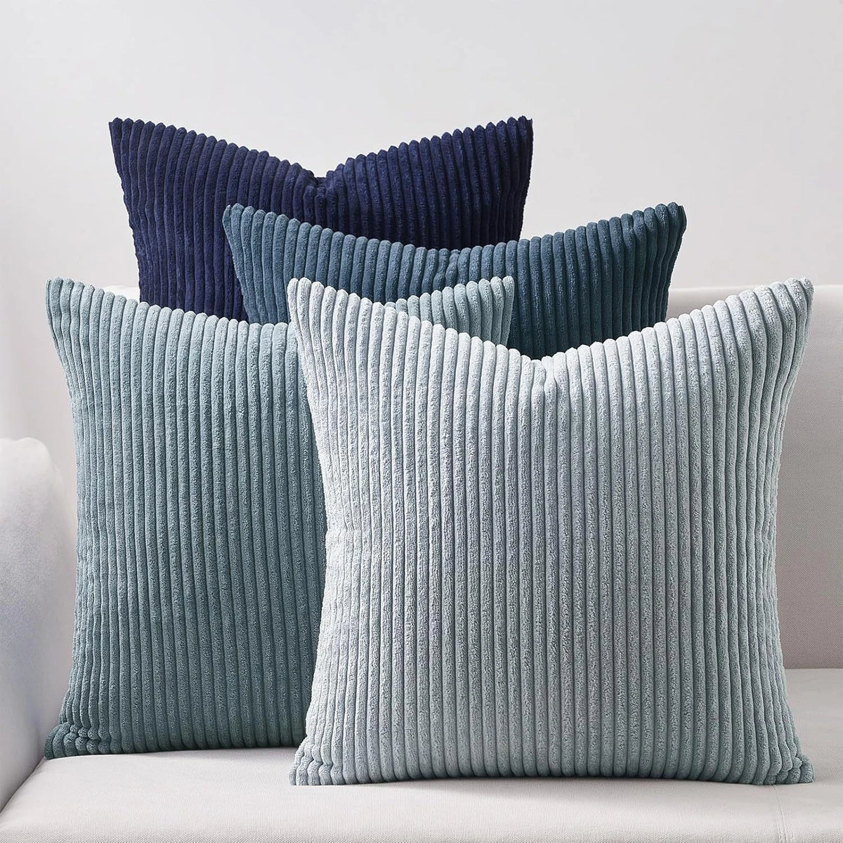A set of four textured throw pillows in shades of blue and gray on a white sofa.