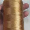 A spool of golden brown high tenacity polyester sewing thread with a yellow plastic core is held in a hand.