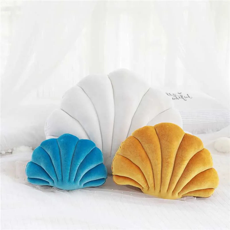 A pair of velvet stuffed sofa cushions shaped like seashells in blue and gold resting on white fabric.